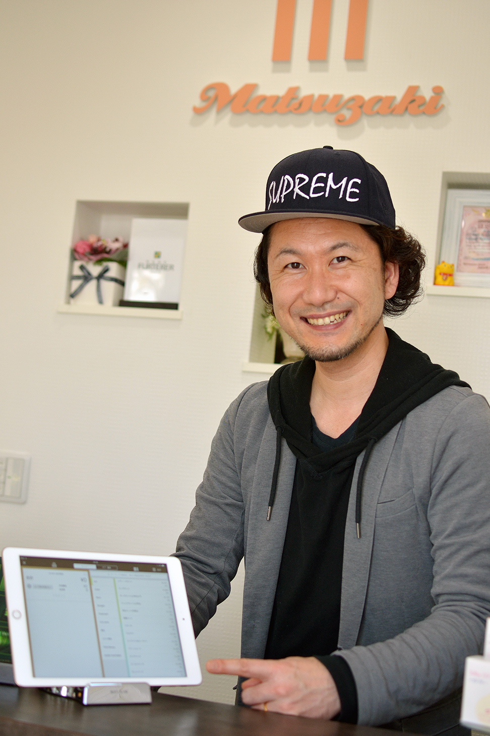 松崎オーナーが笑顔で指すのは美容室で使用中のiPadPOSレジ「ユビレジ」